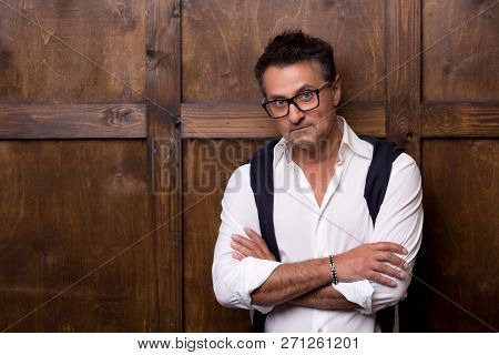 Serious Calm Dark Haired Man Wearing Glasses And Standing Against The Wooden Wall While Having His A