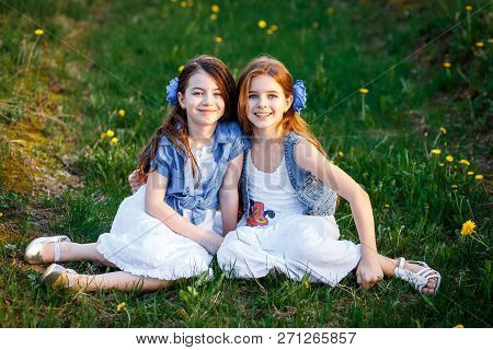 Young Girls In White Dresses In The Garden With Apple Trees Blosoming At The Sunset. Two Friends Hug