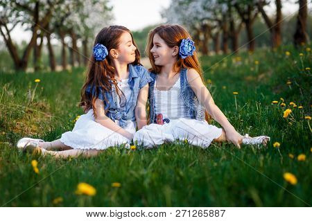 Young Girls In White Dresses In The Garden With Apple Trees Blosoming At The Sunset. Two Friends Hug
