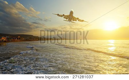 Passenger Plane Is Taking Off On The Background Of The Sea Shore At Dawn And Sunset