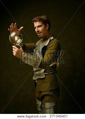 Medieval Knight With Lamp On Dark Studio Background. Portrait In Low Key Of Brutal Man In Tradishion