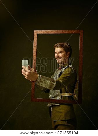 Medieval Knight With Mobile Phone On Dark Studio Background. Portrait In Low Key Of Brutal Man In Tr