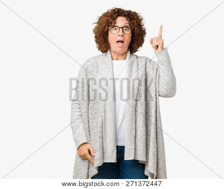 Beautiful middle ager senior woman wearing jacket and glasses over isolated background pointing finger up with successful idea. Exited and happy. Number one.