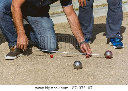 Senior People Measuring Distance In Petanque Game In A Park Outside