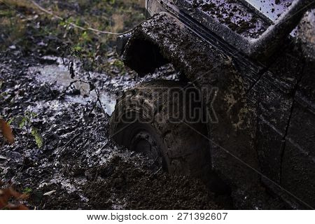 Fragment Of Car Stuck In Dirt, Close Up. Wheel In Deep Puddle Of Mud Overcomes Obstacles. Offroad Ti