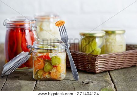 Autumn seasonal pickled vegetables in glass jars, on rustic wooden background.