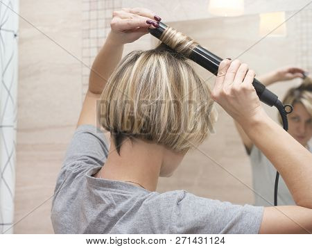 Young Female Curling Hair With A Hair Styler, Looking At The Mirror, Indoor Close-up
