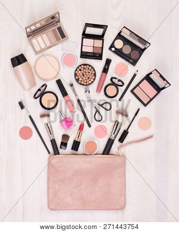 Makeup cosmetics and accessories and an open bag on white wooden background, top view with copy space