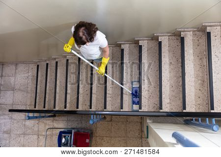 Young Female Janitor Cleaning Staircase With Mop