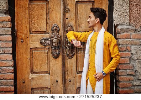 Indian Stylish Man In Yellow Traditional Clothes With White Scarf Posed Outdoor Against Old Gates.