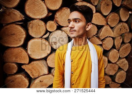 Indian Stylish Man In Yeallow Traditional Clothes With White Scarf Posed Outdoor Against Wooden Stum