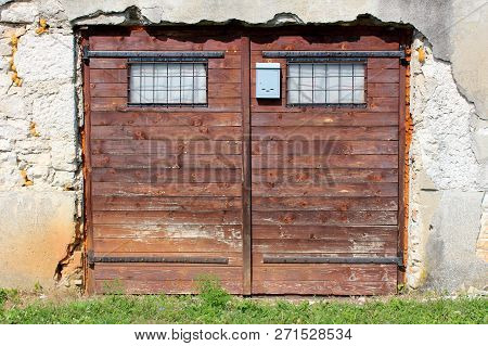 Garage Doors Made Of Small Wooden Boards With Faded Brown Color And Two Small Windows Protected With