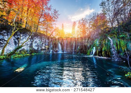 Amazing waterfall with pure blue water in Plitvice lakes. Orange autumn forest on background. Plitvice National Park, Croatia. Landscape photography