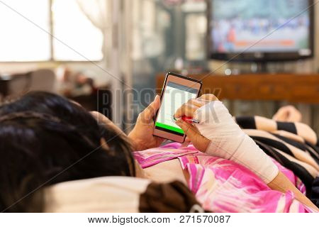 Senior Patient Hand Injured With Bandage Lying Down And Using Cell Phone.