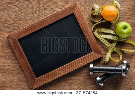 Top View Of Blank Wooden Chalk Board, Fruits, Dumbbells And Measuring Tape, Dieting And Healthy Life