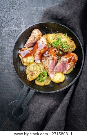 Fried suckling pig fillet with potatoes and hot sauce offered as top view in a modern design cast- iron pan with herbs 