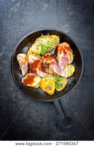 Fried suckling pig fillet with potatoes and hot sauce offered as top view in a modern design cast- iron pan with herbs 
