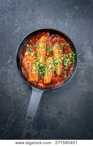Fried suckling pig fillet in hot tomato chili sauce offered as top view in a modern design cast- iron pan with herbs 