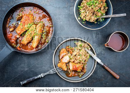 Fried suckling pig fillet with stir fried rice in hot tomato chili sauce offered as top view in a modern design cast- iron pan with herbs 