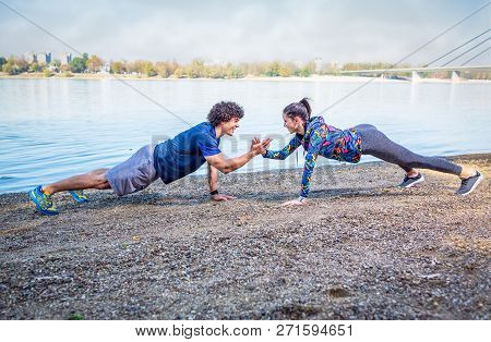 Sportswoman And Sportsman Giving High Five To Each Other While Doing Push-ups Outdoors