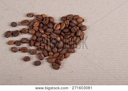Brown Roasted Coffee Beans Forming A Heart Shape With Traces On A Grey Background Of Ribbed Paper.