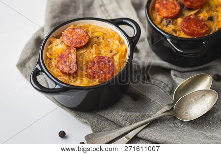 Slovak Christmas National Cabbage Soup In Two Small Black Pots With Sausage On The Tablecloth Backgr