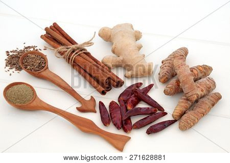 Spice selection used for helping with weight loss and fat busting with fresh and dried turmeric, cumin, ginger, chilli, cinnamon and gymnema sylvestre use to suppress appetite, on white wood.