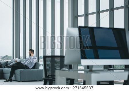 Young Asian Businessman Using Smart Phone On Sofa There Are Document In Hand In The Office Where The