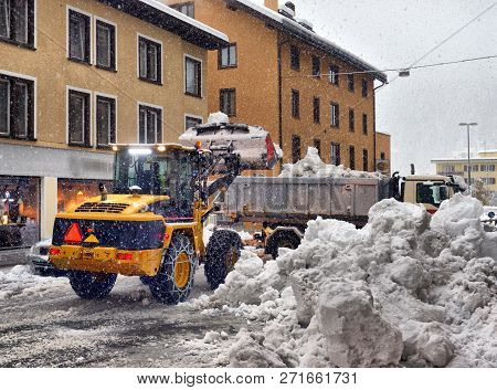 Snow Cleaning Tractor Snow-removal Machine Loading Pile Of Snow On A Dump Truck. Snow Plow Outdoors 