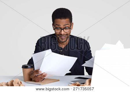 Shocked Dark Skinned Man Carries Many Papers, Looks Surprisingly Through Spectacles, Wears Formal Cl