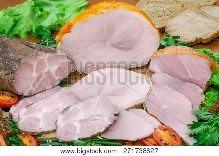 Assortment Of Meat Products Including Ham And Sausages With Greenary And Spices On Wooden Table Clos