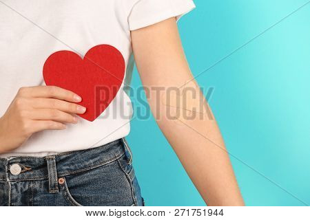 Woman Holding Heart Near Hand With Adhesive Plasters Against Color Background, Closeup. Blood Donati
