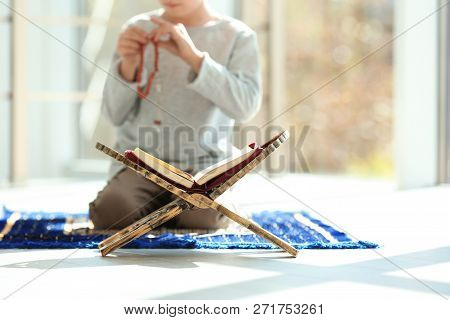 Book Stand With Koran And Little Muslim Boy Praying Indoors