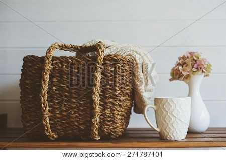 Cozy Winter Interior Details In White And Brown Tones. Basket With Knitted Sweater And Cup Of Coffee