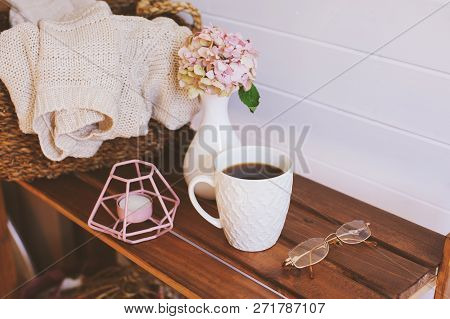 Cozy Winter Interior Details In White And Brown Tones. Basket With Knitted Sweater And Cup Of Coffee