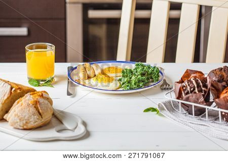 Breakfast Served With Fried Eggs, Salad, Muffins And Orange Juice On White Wooden Table In The Kitch