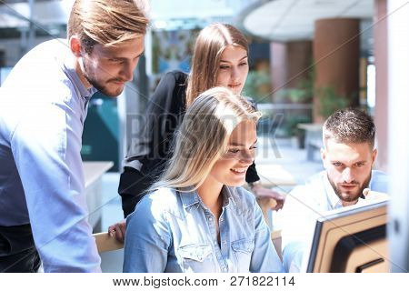 Group Of Young People In Casual Wear Sitting At The Office Desk And Discussing Something While Looki