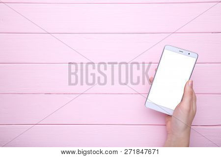 Female Hands Holding Mobile Phone With Blank Screen On Pink Wooden Table. Smartfone White