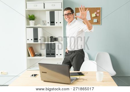 Business, Office, People Concept - Handsome Man In Glasses Stands In The Office Near A Computer And 