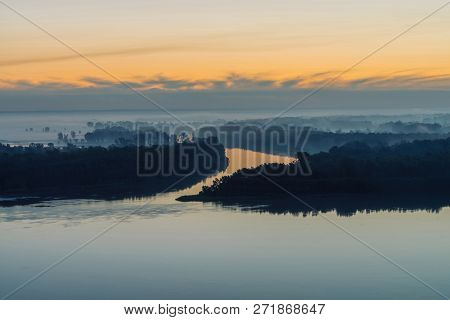 Broad River Flows Along Coast With Forest Under Thick Fog. Early Blue Sky Reflected In Water. Yellow
