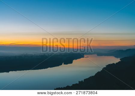 View From High Shore On Broad River. Riverbank With Forest Under Thick Fog. Dawn Reflected In Water.