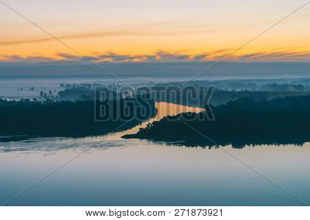 Early Blue Sky Reflected In River Water. Riverbank With Forest Under Predawn Sky. Yellow Stripe In P