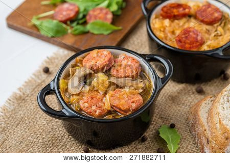 Slovak Christmas National Cabbage Soup In Two Small Black Pots With Sausage On The Tablecloth Backgr