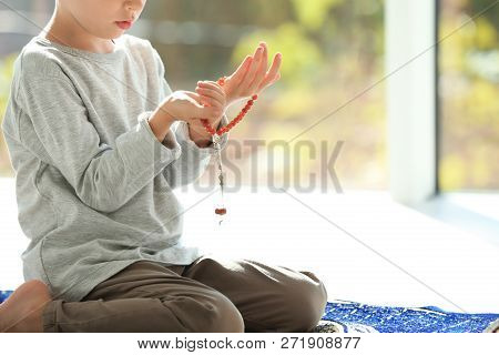 Little Muslim Boy With Misbaha Praying On Rug Indoors, Closeup. Space For Text