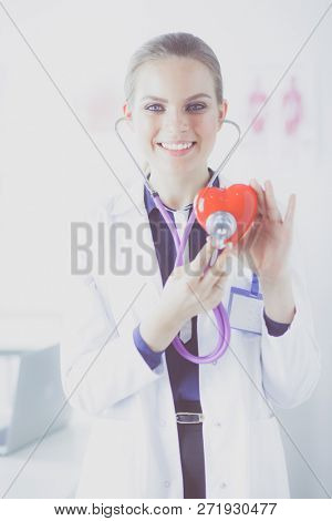 A doctor with stethoscope examining red heart, isolated on white background