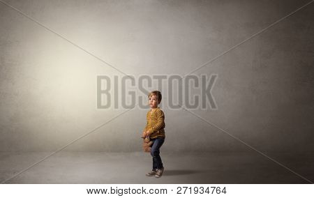 Little waggish kid staying alone in a big empty room with his plush