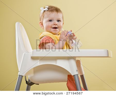 Niña feliz sentado en la silla alta con botella