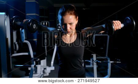 The Girl Is Engaged In The Gym. Exercise On The Deltoid Muscles With A Dumbbell.