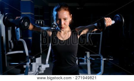 The Girl Is Engaged In The Gym. Exercise On The Deltoid Muscles With A Dumbbell.
