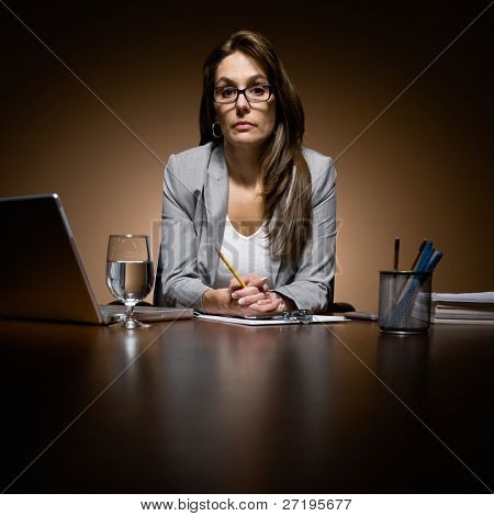 Alvorlige, ulykkelig forretningskvinde arbejder sent på skrivebord med laptop og papirarbejde